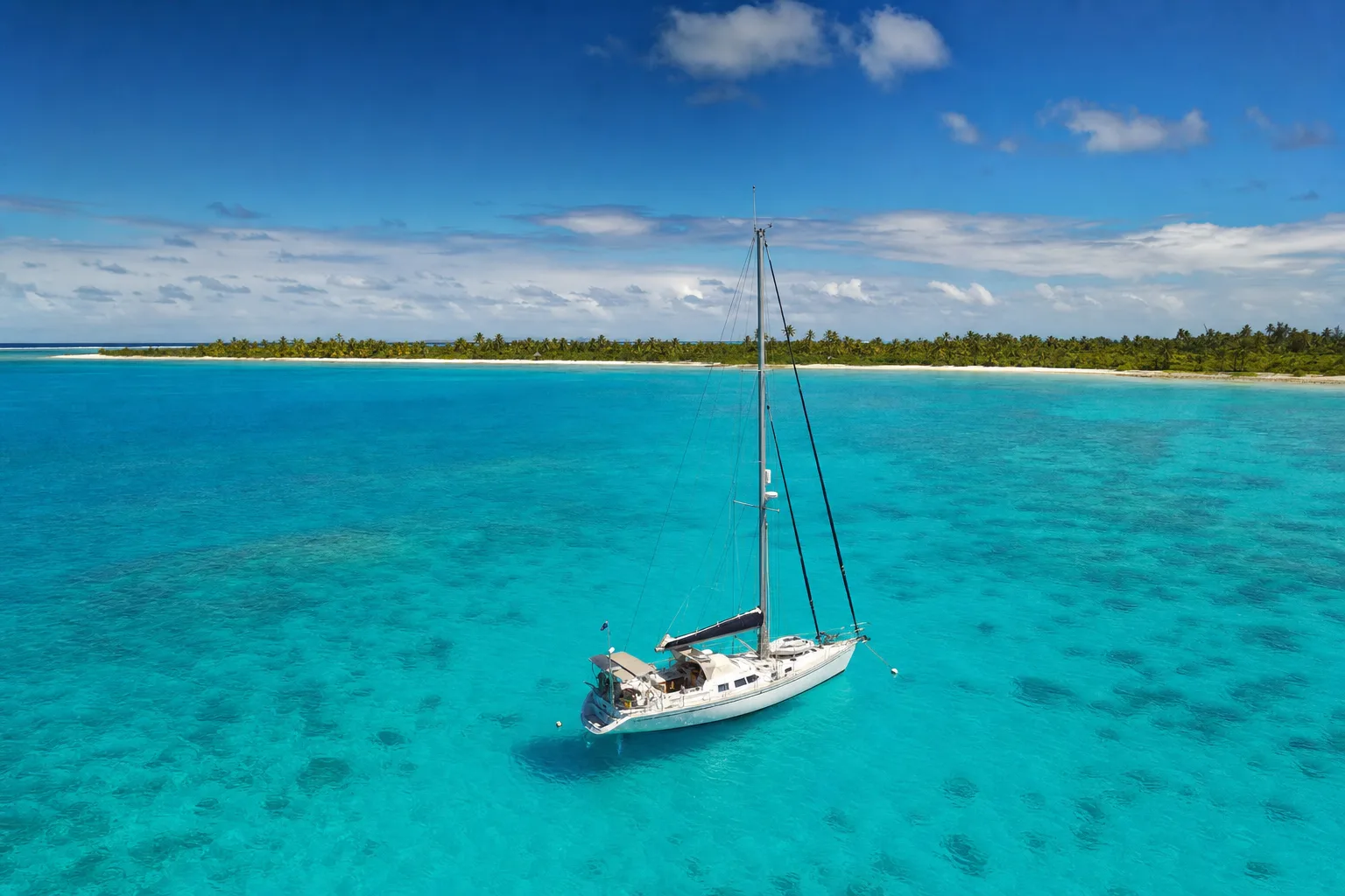 A yacht anchored alone off an empty palm-fringed atoll